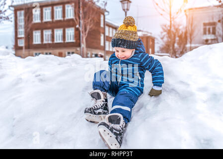 Petit garçon enfant 3-5 ans. Siège de la neige couverte de neige, patins city park de l'hiver. Premiers pas sur la patinoire. Espace libre pour le texte. En salopette bleue et Banque D'Images