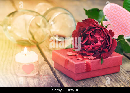 Concept de la Saint-Valentin. Red Rose, boîte cadeau, bougie allumée et deux verres de vin sur une table en bois rustique. Focus sélectif. Banque D'Images