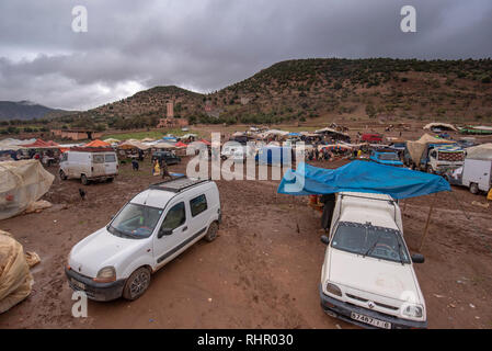 Vue d'un souk berbère bazar marché hebdomadaire tenu dans la campagne dans la boue et par mauvais temps. Une scène animée de locaux et de véhicules au Maroc Banque D'Images