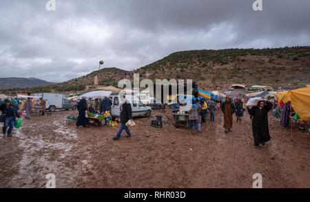 Vue d'un souk berbère bazar marché hebdomadaire tenu dans la campagne dans la boue et par mauvais temps. Une scène animée de locaux et de véhicules au Maroc Banque D'Images