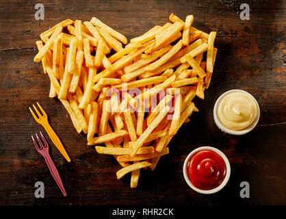 En forme d'coeur portion de frites avec des trempettes, vinaigrettes ou sauces dans de petits bols à côté sur bois Banque D'Images