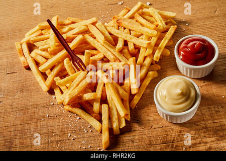 Et salé en forme de coeur aguerri au service de croustilles de pommes de terre frites avec de la moutarde et du ketchup sur bois avec fourchette en plastique Banque D'Images