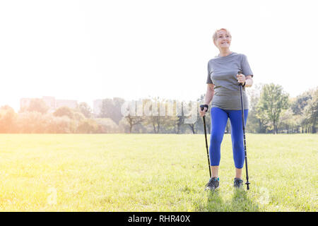 Smiling senior woman en utilisant les bâtons de trekking en marchant dans le parc Banque D'Images