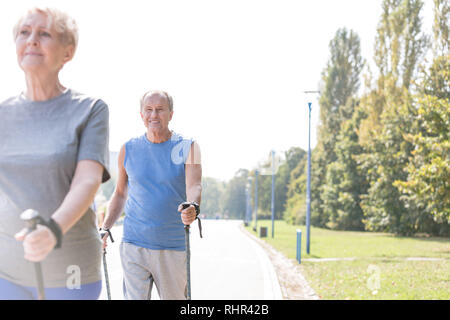 Smiling senior man en utilisant les bâtons de trekking en marchant avec femme dans park Banque D'Images