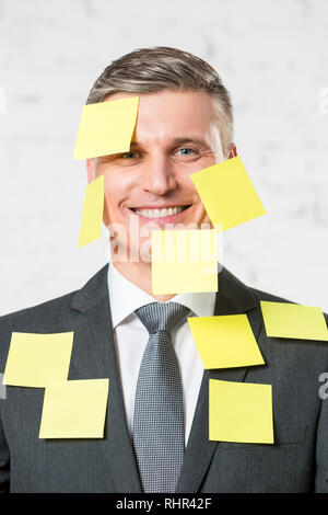 Portrait of smiling businesswoman with blank notes adhésives jaunes sur le visage et le costume at office Banque D'Images