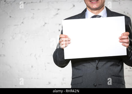 Portrait of businessman holding blank placard en position debout contre un mur en brique blanche Banque D'Images