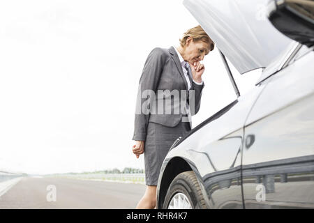 Inquiets businesswoman looking at ventilation voiture sur route contre sky Banque D'Images