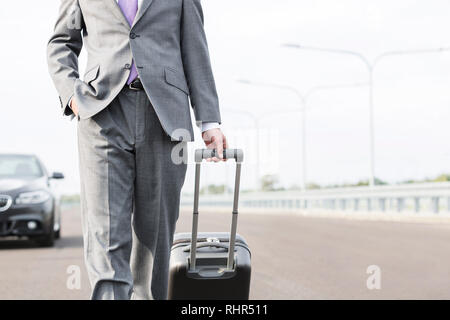 Portrait of businessman walking with suitcase on road against sky Banque D'Images