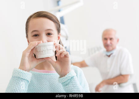 Portrait de jeune fille montrant un dentier contre dentiste assis dans une clinique dentaire Banque D'Images