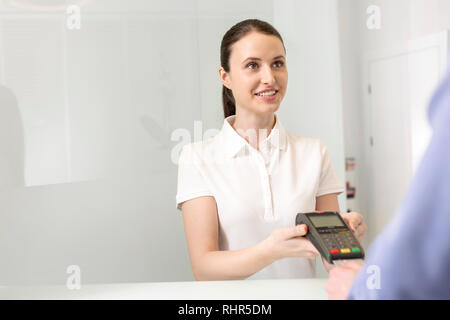Smiling young patient de payer des frais par carte de crédit à la caisse en clinique Banque D'Images