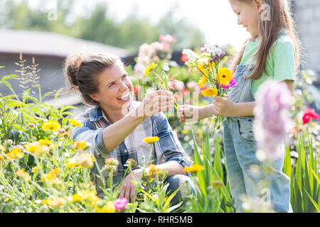 Smiling mother donnant des fleurs en fille tout en faisant du jardinage à la ferme Banque D'Images