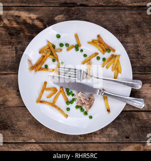 Les restes de frites petits pois et le poulet sur une plaque à l'aide d'un couteau et fourchette sur un fond de bois rustique Banque D'Images