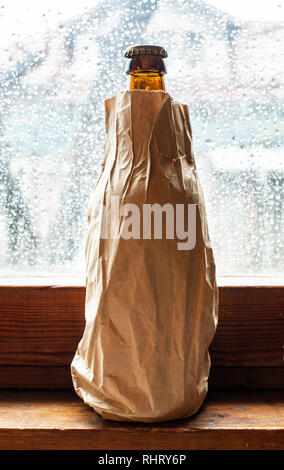 Bouteille avec de l'alcool dans un pack brown papier placé à la fenêtre au jour de pluie. L'emballage du papier froissé. Bouteille cachés de l'alcool en papier. Concept pour voler Banque D'Images