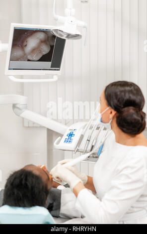 Avec une inspection caméra macro dentaire et affiche le résultat sur le moniteur. Jeune femme dentiste traitant des traitements de canaux dans la clinique dentaire. Man Banque D'Images