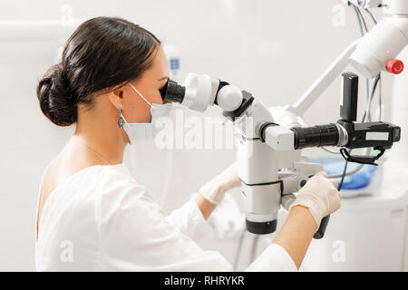 Femme dentiste utilisateur avancé, outils de dentiste. Recherche dans l'objectif d'un microscope tout en examinant ses dents. Les patients dans une clinique dentaire office Banque D'Images