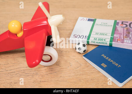 Ballon de soccer et une montagne d'argent d'une valeur nominale de cinq cents euros avec un passeport biométrique à l'avion jouet sur une table en bois. Banque D'Images