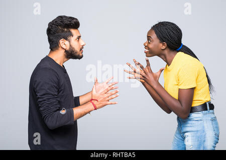 Heureux surpris jeune couple interracial vêtu de vêtements identiques et les lunettes en gardant ses poings fermés à leurs visages, des cris, de la bouche d'ouverture Banque D'Images