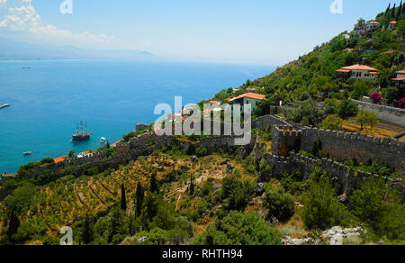 Les murs de la forteresse et les maisons dispersées sur la piste verte en descendant vers la mer bleue de la Méditerranée avec des montagnes de brume à l'horizon en ligne Banque D'Images