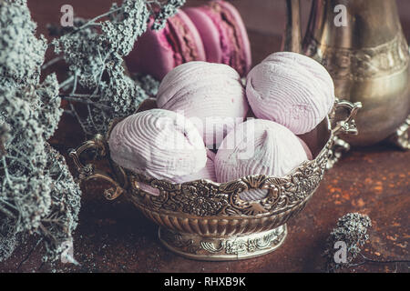 Des guimauves et macarons sur plaque de métal avec de petites fleurs blanches et de thé composition appareils sur fond de bois. Selective focus Banque D'Images