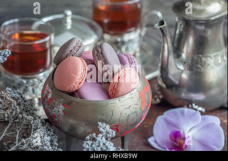 Des petits macarons sur plaque de métal avec de petites fleurs blanches et de thé composition appareils sur fond de bois. Banque D'Images