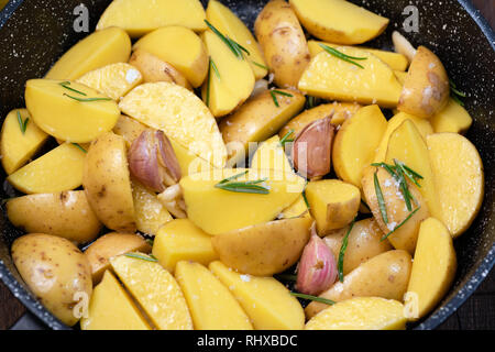 Les quartiers de pommes de terre au romarin, l'ail et de sel de mer dans une poêle en fonte, vue rapprochée Banque D'Images