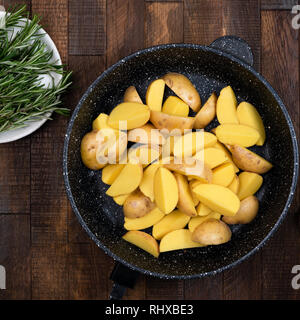 Les quartiers de pommes de terre dans la poêle en fonte avec des herbes de romarin, huile d'olive et sel de mer. Vue de dessus de table Banque D'Images