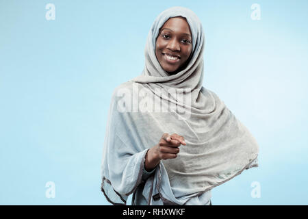 La belle jeune fille musulmane d'Afrique noire portant le hijab gris bleu au studio. Elle debout avec un sourire heureux sur son visage. Les émotions humaines, l'expression faciale concept. Couleurs tendance Banque D'Images