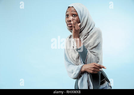 Secret, gossip concept. Jeune femme africaine whispering a secret derrière sa main. La femme isolé sur fond bleu à la mode studio. Jeune femme émotionnelle. Les émotions humaines, l'expression faciale concept. Banque D'Images