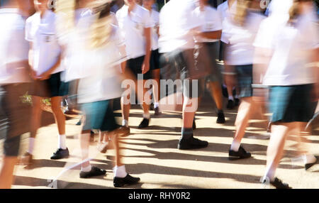 Grand nombre d'élèves, garçons et filles portant des uniformes propres se déplaçant entre les classes dans un environnement haute cour de l'école. heavy de flou. Banque D'Images