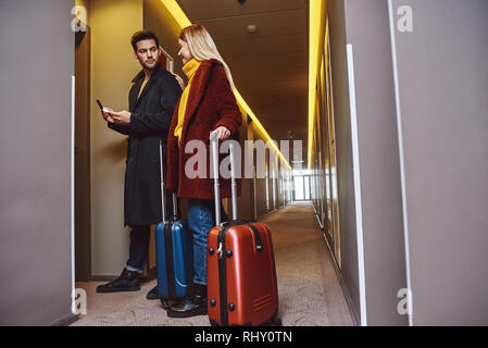 S'installer dans la salle. Jeune couple près de l'entrer dans la chambre d'hôtel avec leurs bagages et d'avoir un chat. Vue de côté Banque D'Images