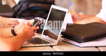 Portrait d'un élève du secondaire à une table ou sur un bureau mobile cell phone texting tout en étudiant. Fond d'écran de l'ordinateur portable de l'ordinateur et des livres. Banque D'Images