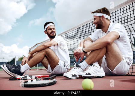 Deux beaux les joueurs de tennis sont assis sur le terrain après le match, parler et sourire à l'autre Banque D'Images