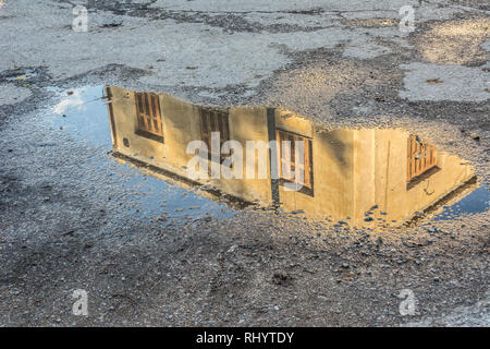 Bâtiment abandonné avec volets jaunes reflète dans une flaque d'eau après la pluie à Athènes, Grèce Banque D'Images
