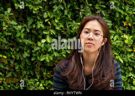 Young Asian woman avec écouteurs sur fond de plantes vertes. Banque D'Images