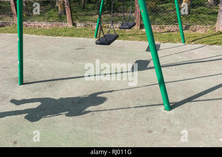 Ombre d'un petit enfant assis sur une balançoire dans un parc de jeu Banque D'Images