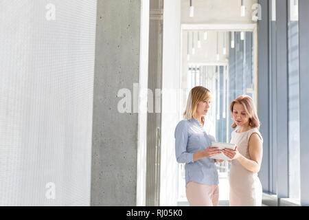 Businesswomen discussing sur digital tablet in office corridor Banque D'Images