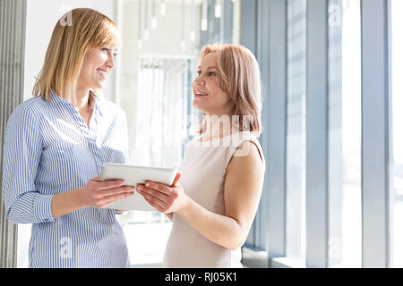 Businesswomen discussing sur digital tablet in office corridor Banque D'Images