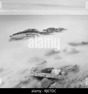 Une longue exposition mer paysage artistique. La lumière, l'eau et des pierres. Le noir et blanc Banque D'Images