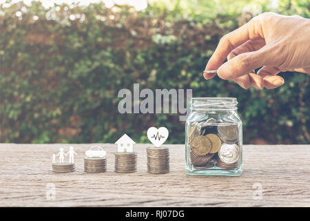 L'argent d'épargne de la vie familiale des concepts. Main tenant une pièce de monnaie sur l'argent dans un bocal en verre et membre de la famille, voiture, maison, sains sur les monnaies. Montre l'enregistrement Banque D'Images