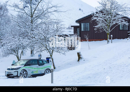 Voiture électrique BMW étant facturé à la station de recharge pour voitures électriques dans la neige point couvert par Clachaig Inn, Glencoe, Highlands, Scotland en hiver Banque D'Images