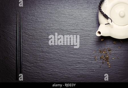 La composition des aliments en Asie avec des baguettes chinoises, théière et sèche thé vert sur une pierre sombre arrière-plan, Vue de dessus, tonique, avec de l'espace libre pour le texte Banque D'Images