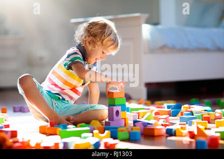 Enfant jouant avec des blocs de jouets. Les jeux des enfants. Petit garçon construire tour de jouets bloc assis sur marbre foncé à sunny chambre blanche. G L'éducation Banque D'Images