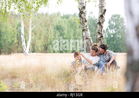 Les parents assis avec sa fille contre l'arbre sur les terres agricoles au champ Banque D'Images