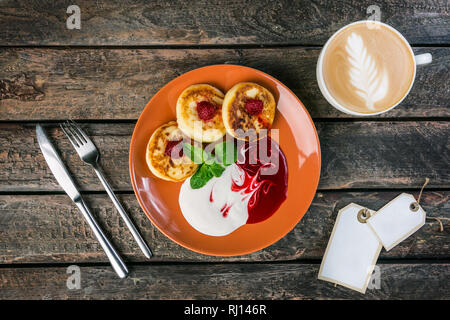 Le petit-déjeuner. Crêpes de fromage cottage avec confiture de framboises et de crème sure, une tasse de café. Servi par les couverts, avec un autocollant pour votre texte. Vue d'en haut Banque D'Images