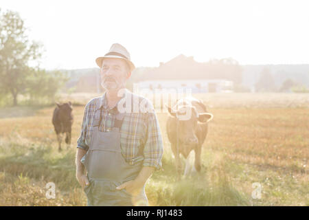 Portrait of senior farmer standing with hands in pockets contre les vaches à la ferme Banque D'Images