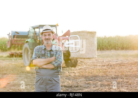 Portrait of farmer standing with arms crossed sur terrain contre l'ensileuse à farm Banque D'Images