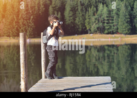 L'enfant créatif, photographe pour enfants (un petit garçon) avec un appareil photo prendre des photos de paysage près de la Lake Banque D'Images