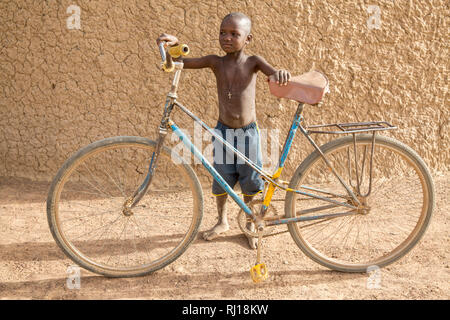 Village de samba, Province de Yako, Burkina Faso : Un jeune garçon avec un adulte vélo. Banque D'Images
