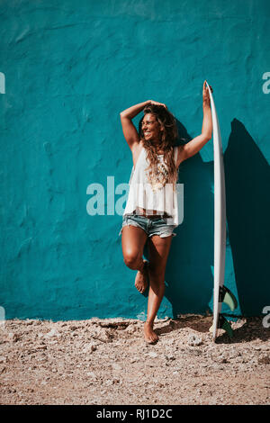 Heureux Surfer Girl with surfboard en face du mur bleu Banque D'Images