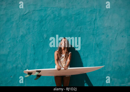 Heureux Surfer Girl with surfboard en face du mur bleu Banque D'Images